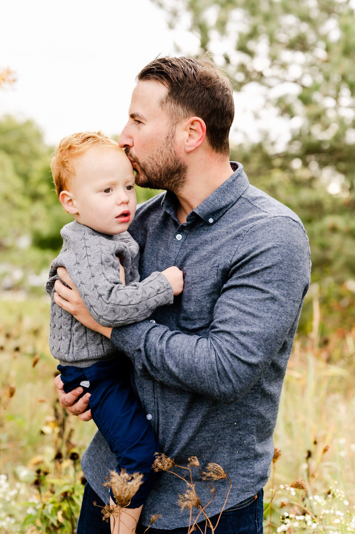 Candid photo of dad kissing toddler in a field of wildflowers near Naperville, IL.