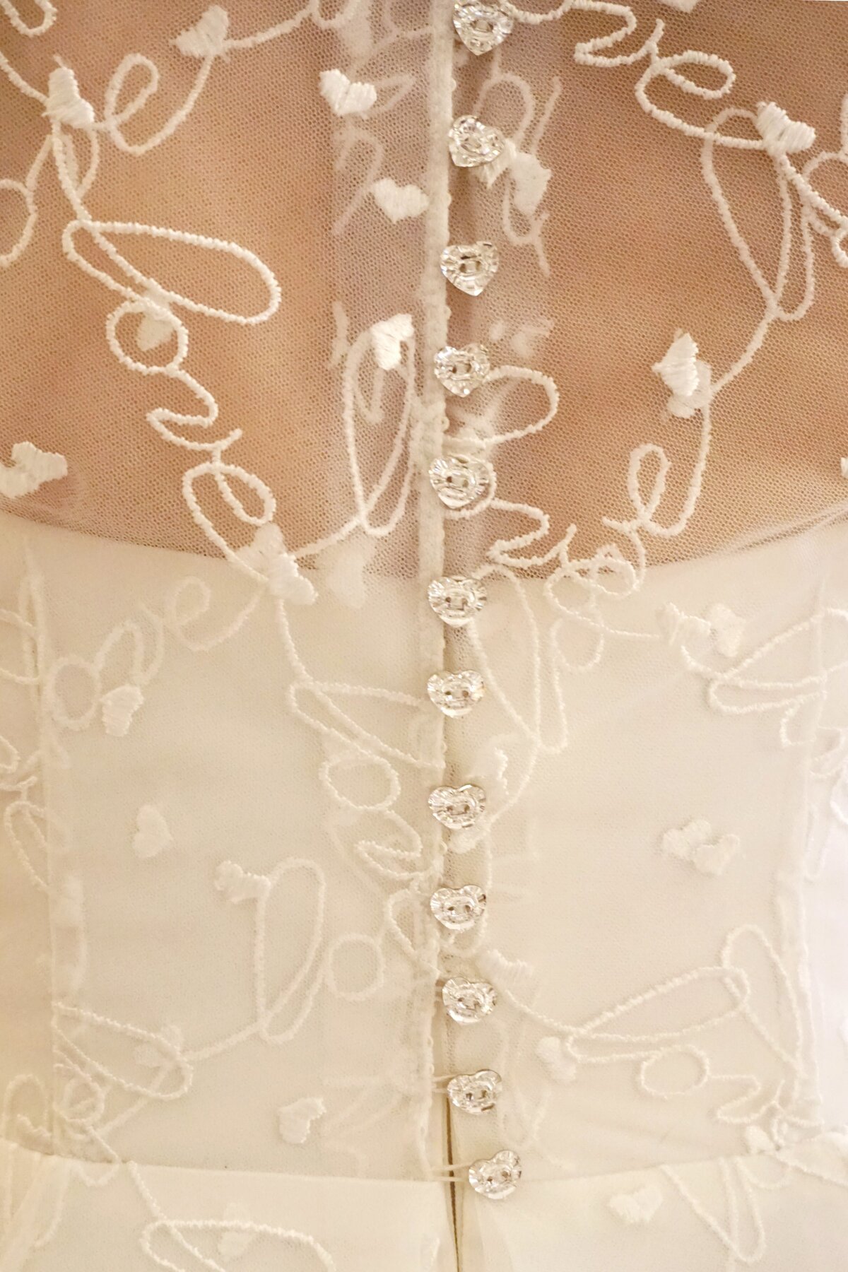 The high back illusion bodice is closed with heart-shaped crystal buttons for a romantic and sparkly touch.