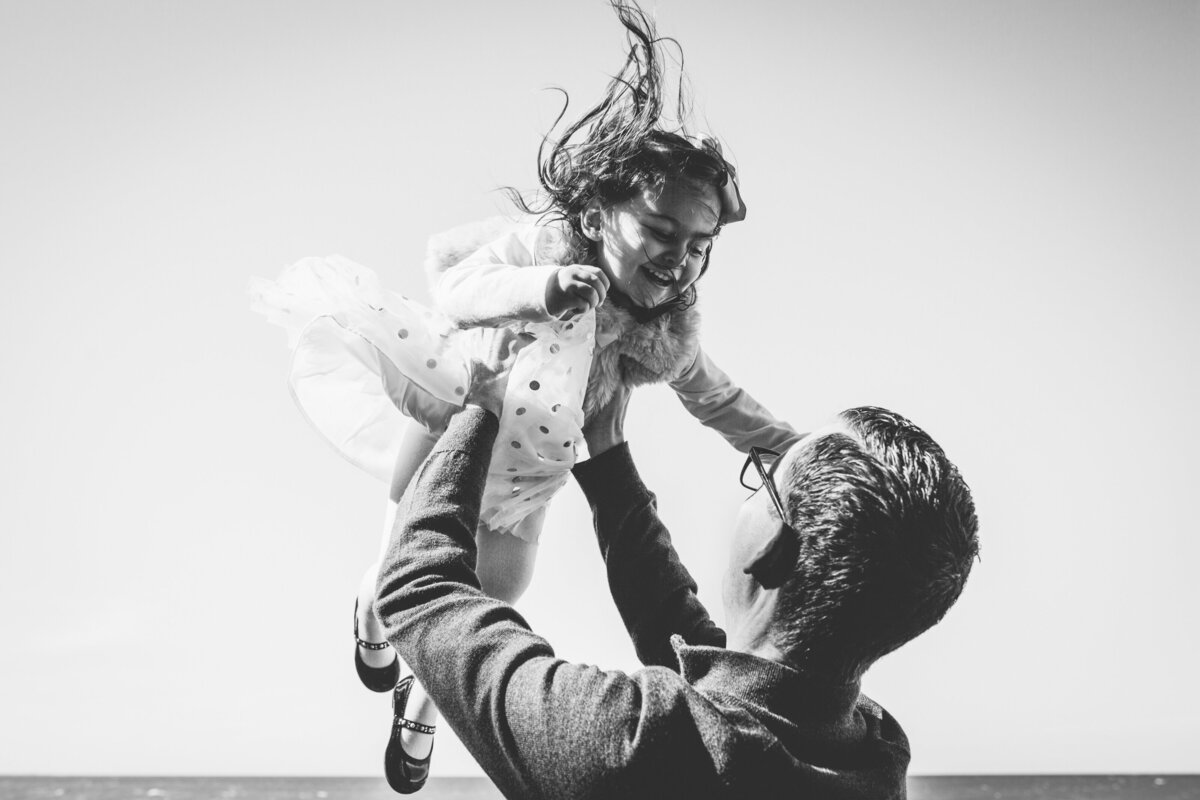 A father lifting his daughter into the air while getting family photos taken.