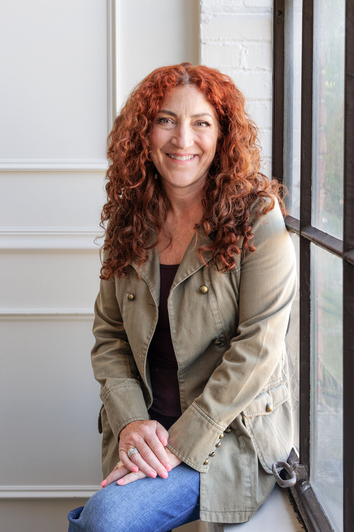 Headshot of women with curly red hair sitting next to window
