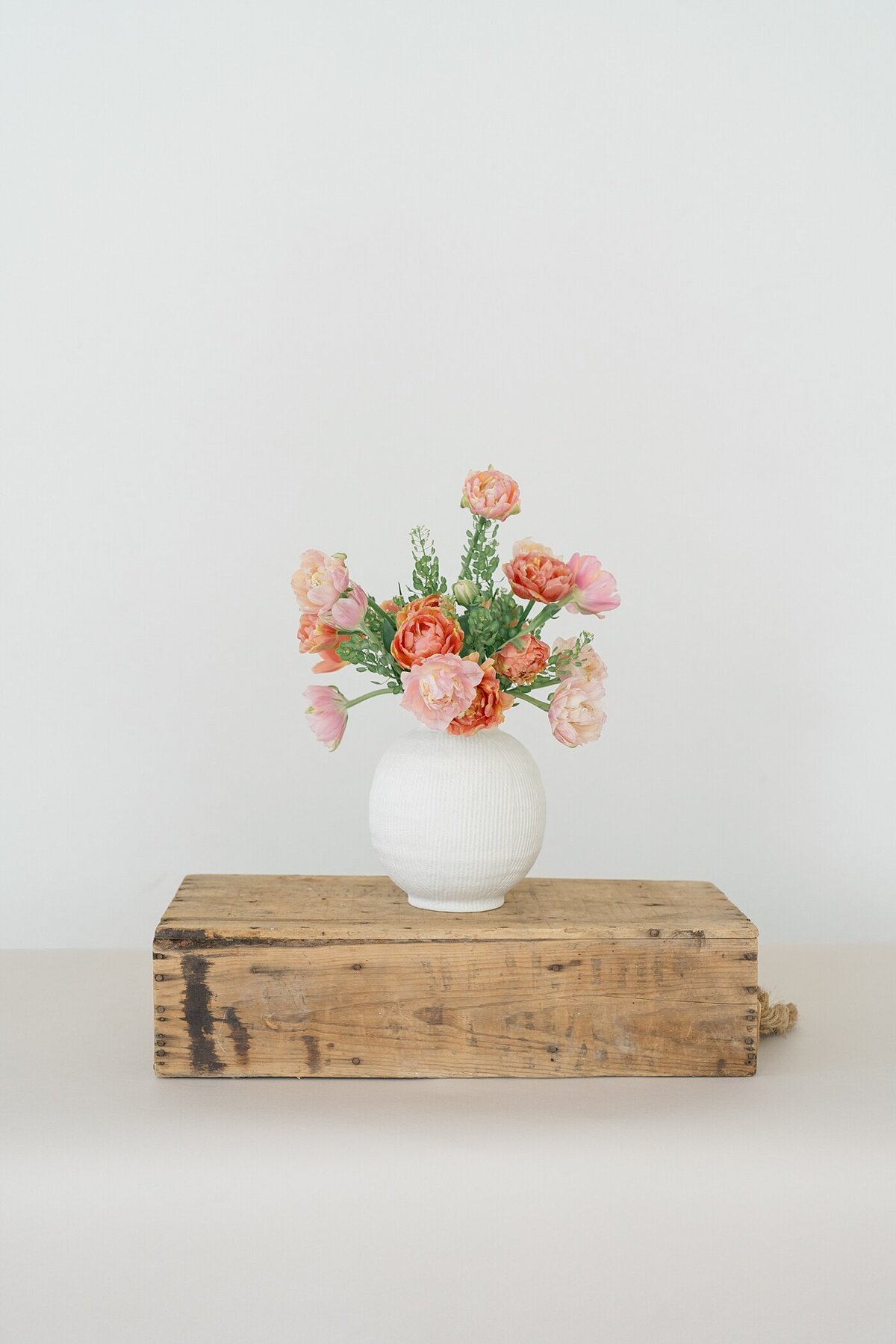 florist makes an arrangement with pink peonies in a white vase on top of a piece of distressed wood photographed by Columbus photographer