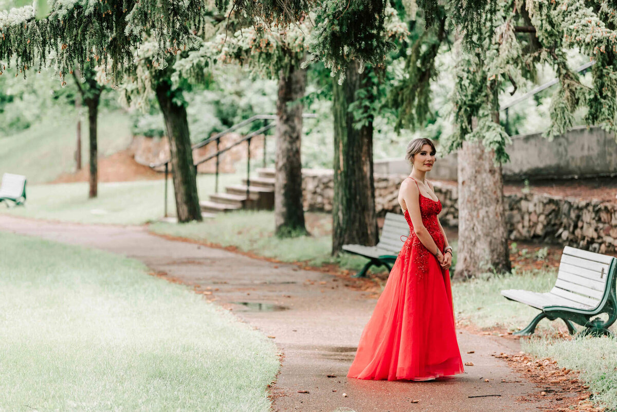 Standing full length by some large trees. 