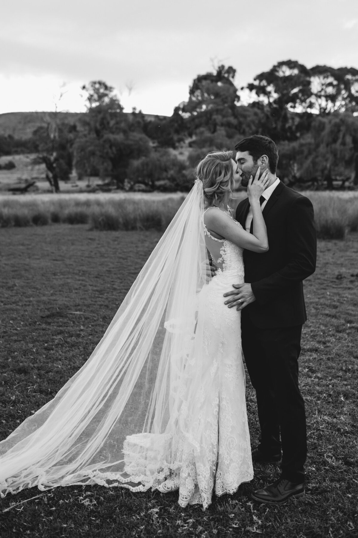Newlyweds sharing an intimate kiss in a field.