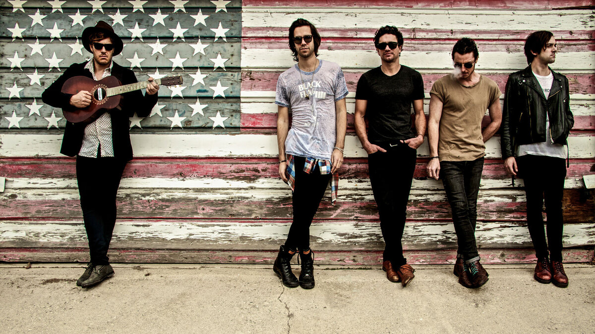 country music band portrait Terraplane Sun members standing against weathered American Flag painted on garage door lead singer holding guitar