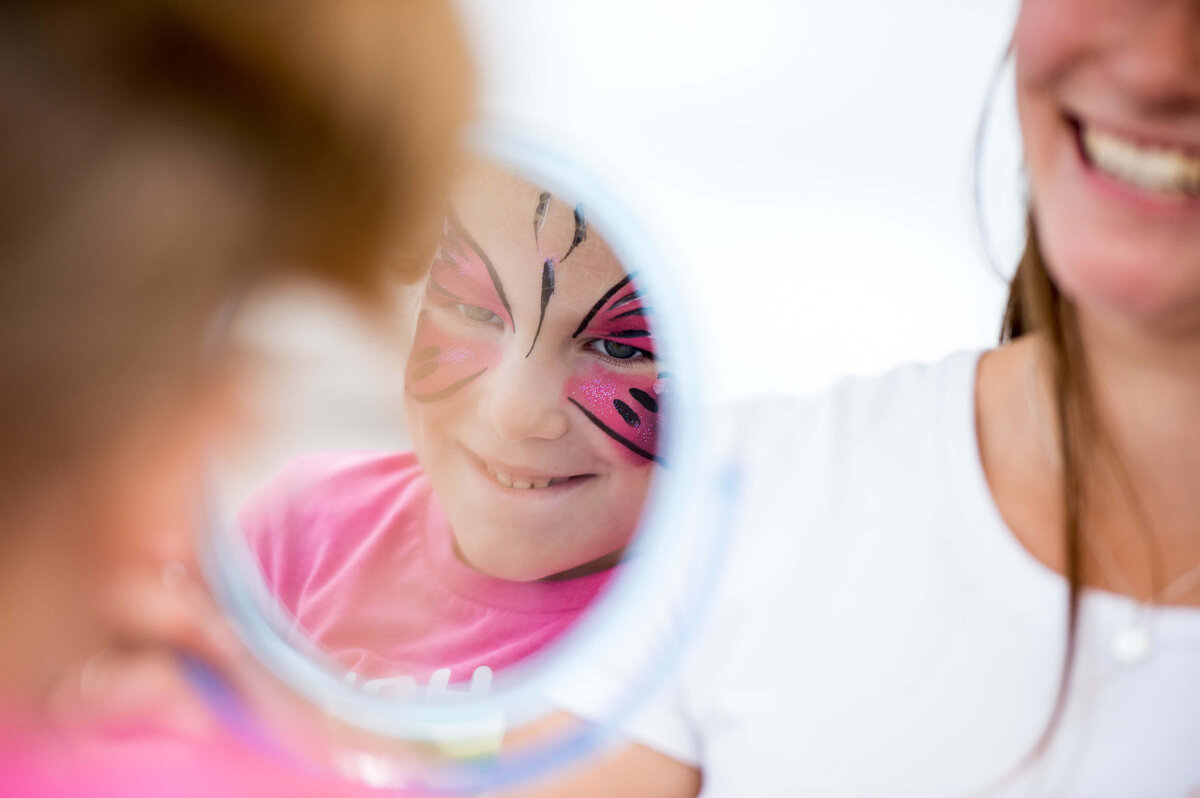 a closeup photo of a little girl in a pink t-shirt with butterfly face paint as part of a corporate children's event.  Captured by Ottawa Event Photographer JEMMAN Photography COMMERCIAL