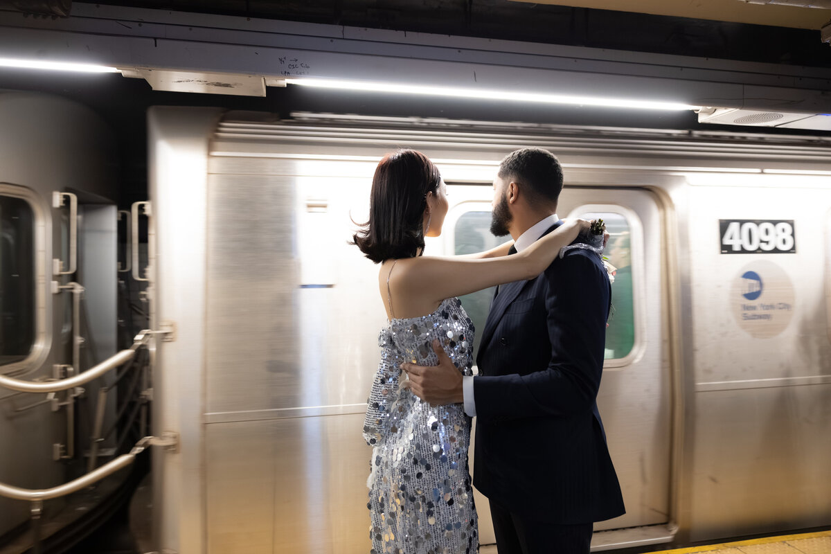 The couple shares a playful laugh on the subway platform, surrounded by the urban energy of New York City.