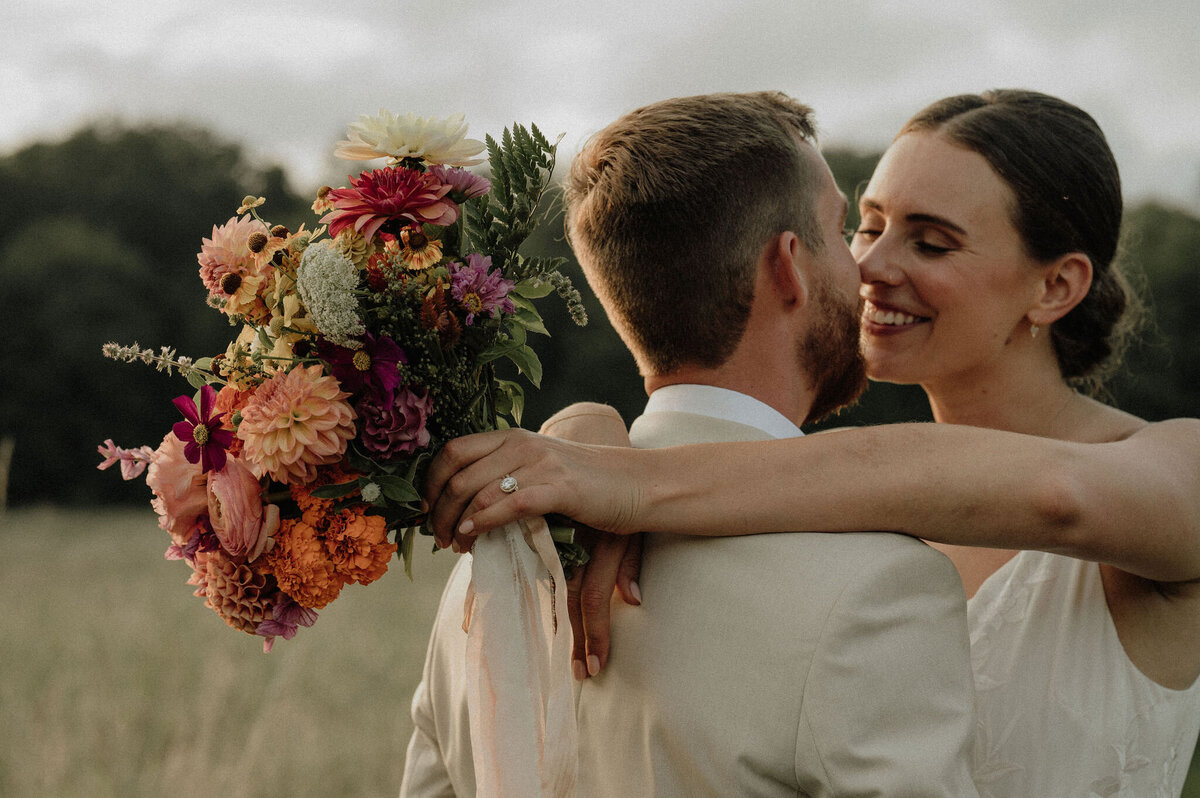 Couple hugging while bride holds florals for Maine wedding