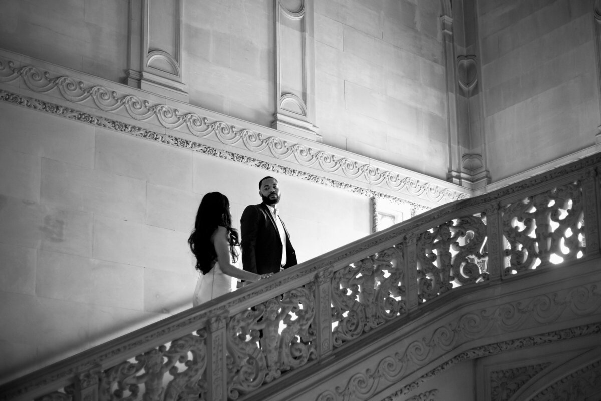 Wedding Photographers in RI | Kelsey Sheehan Photography Timeless Rhode Island Weddings | A couple ascends an ornate staircase in a grand building. The black-and-white image captures an elegant, timeless atmosphere with intricate architectural details.