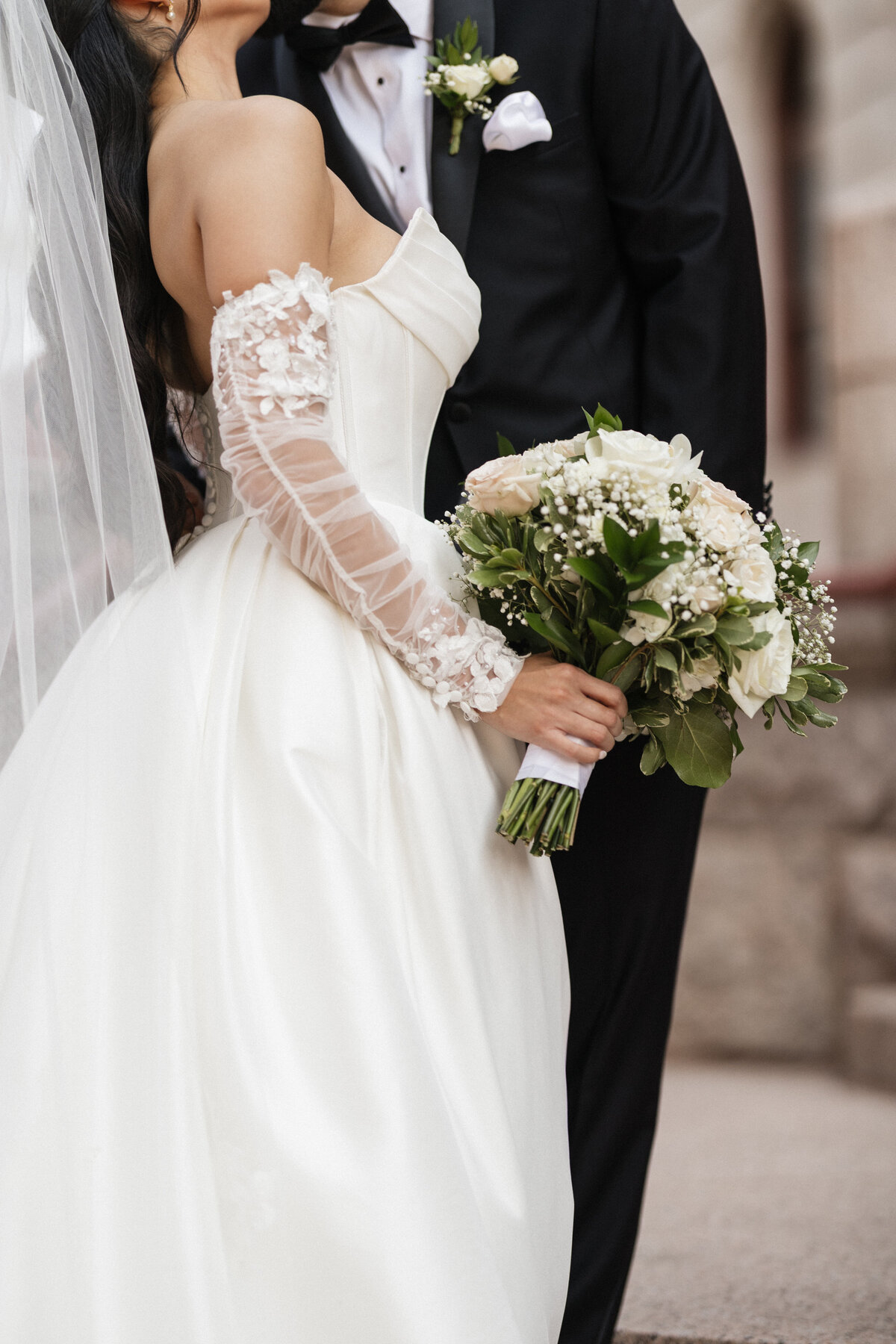 Close up shot of the brides bouquet and dress as she hugs her groom.