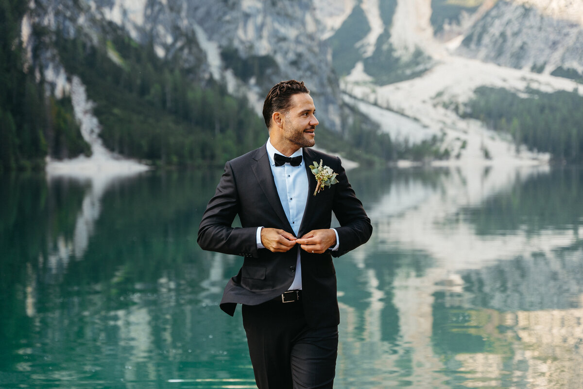 Groom smiling in tuxedo by the lake in the Dolomites