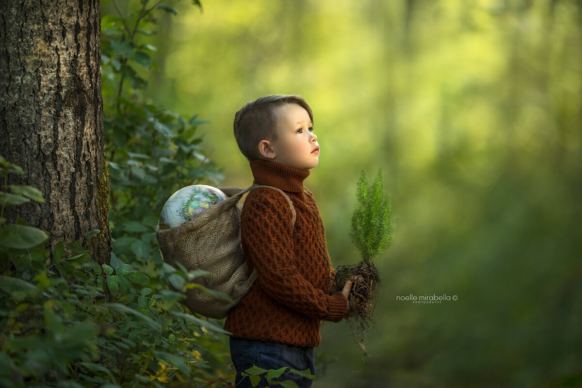 Boy in the forest with a globe on his back and the future in his hands.