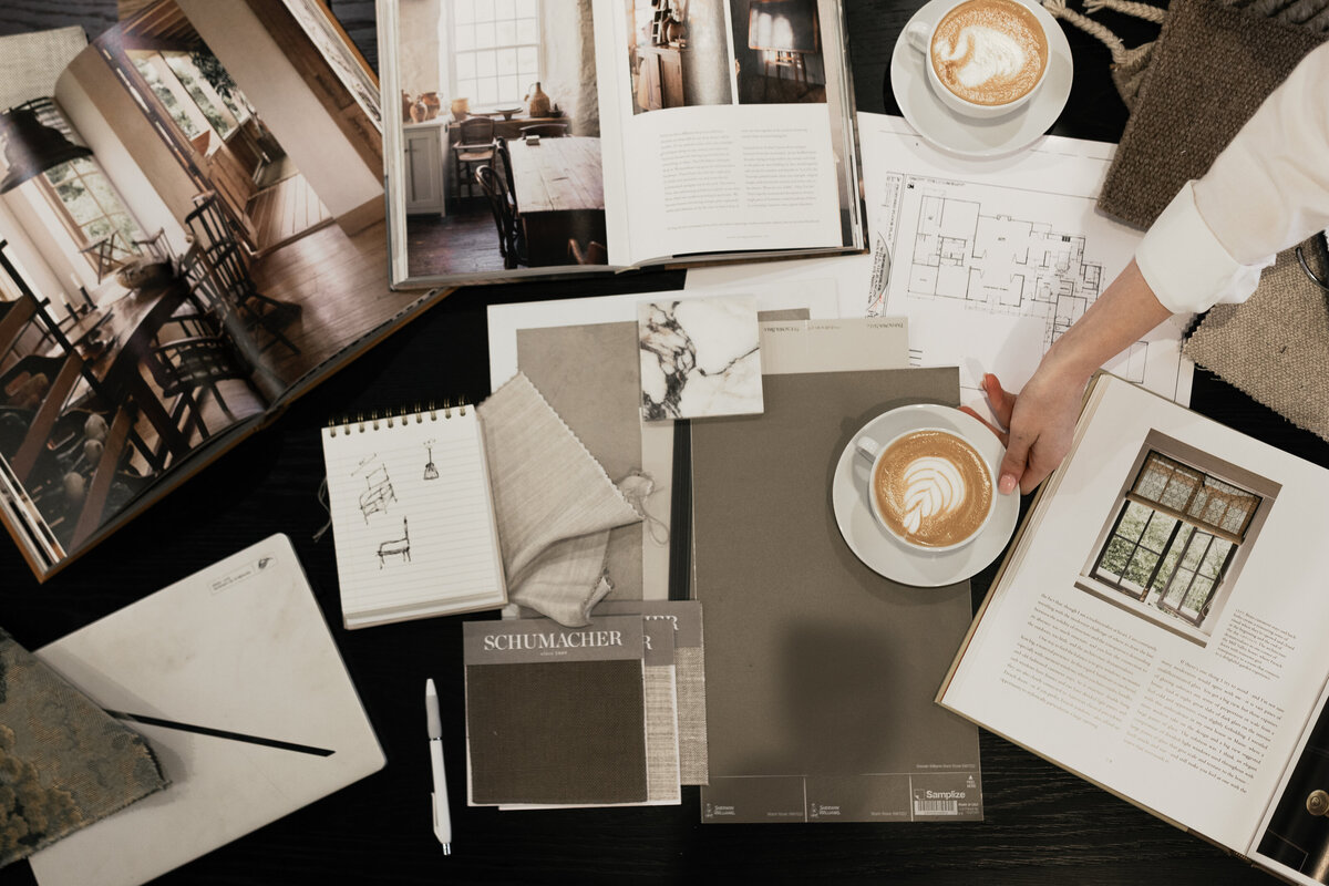 Interior design flatlay featuring mood boards, fabric swatches, architectural sketches, and lattes on a black tabletop — styled editorially by Dani Lacey in Greenville SC for branding photography.