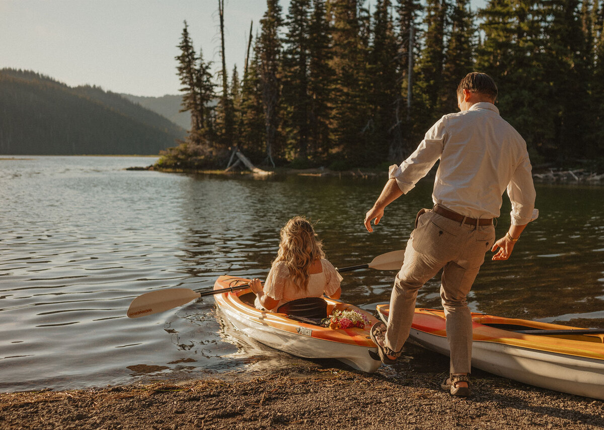 groom pushes his wife out in her kayak for an exclusive elopement session under the sunset sky