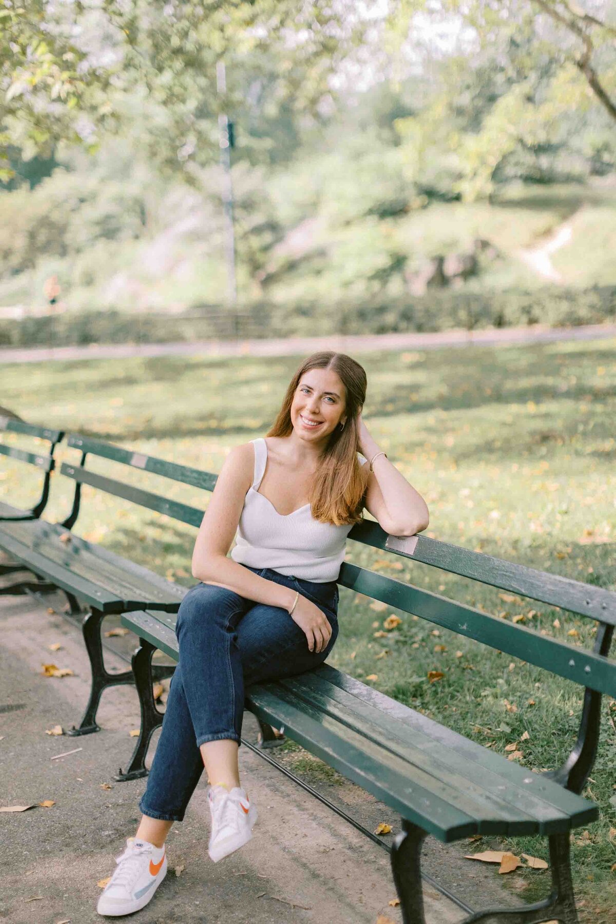 Woman tucking her hair behind her ear and smiling at the camera while sitting in a park