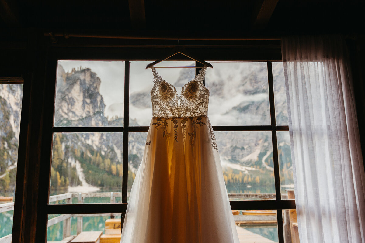 Wedding dress hanging in window with Lago di Braies view