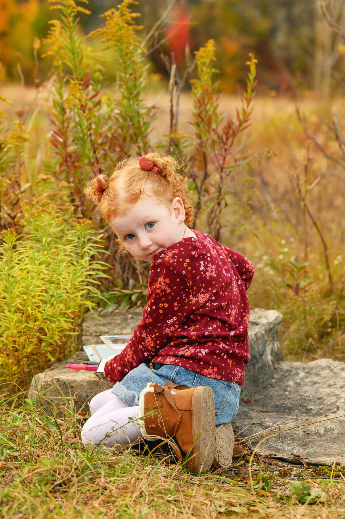 red haired little girl sitting on the ground with a book for her fall family photos in Burlington, ON