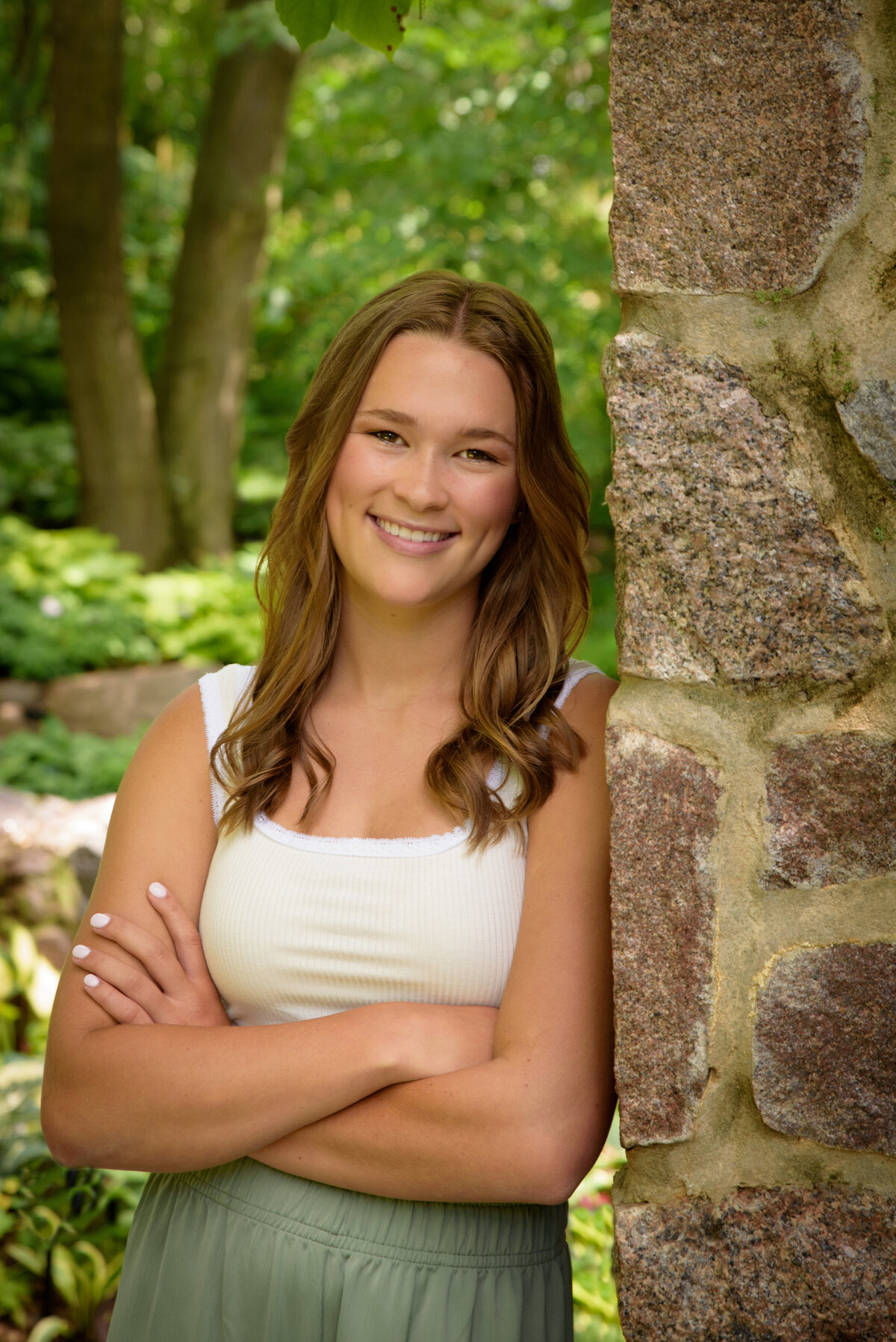 Luxemburg Casco High School senior girl wearing long sage green pants and a white top by stone building in the flower gardens at the Green Bay Botanical Gardens in Green Bay, Wisconsin