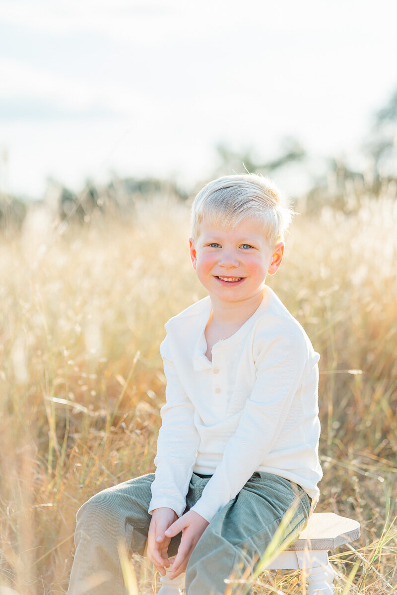 a young boy sits on a stool in a field of golden grass and smiles at his Austin family photographer.