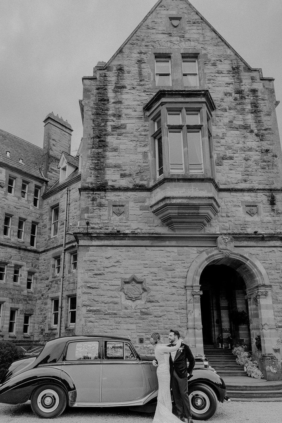 Bride hugging groom in front of a retro car in front of an Ireland castle