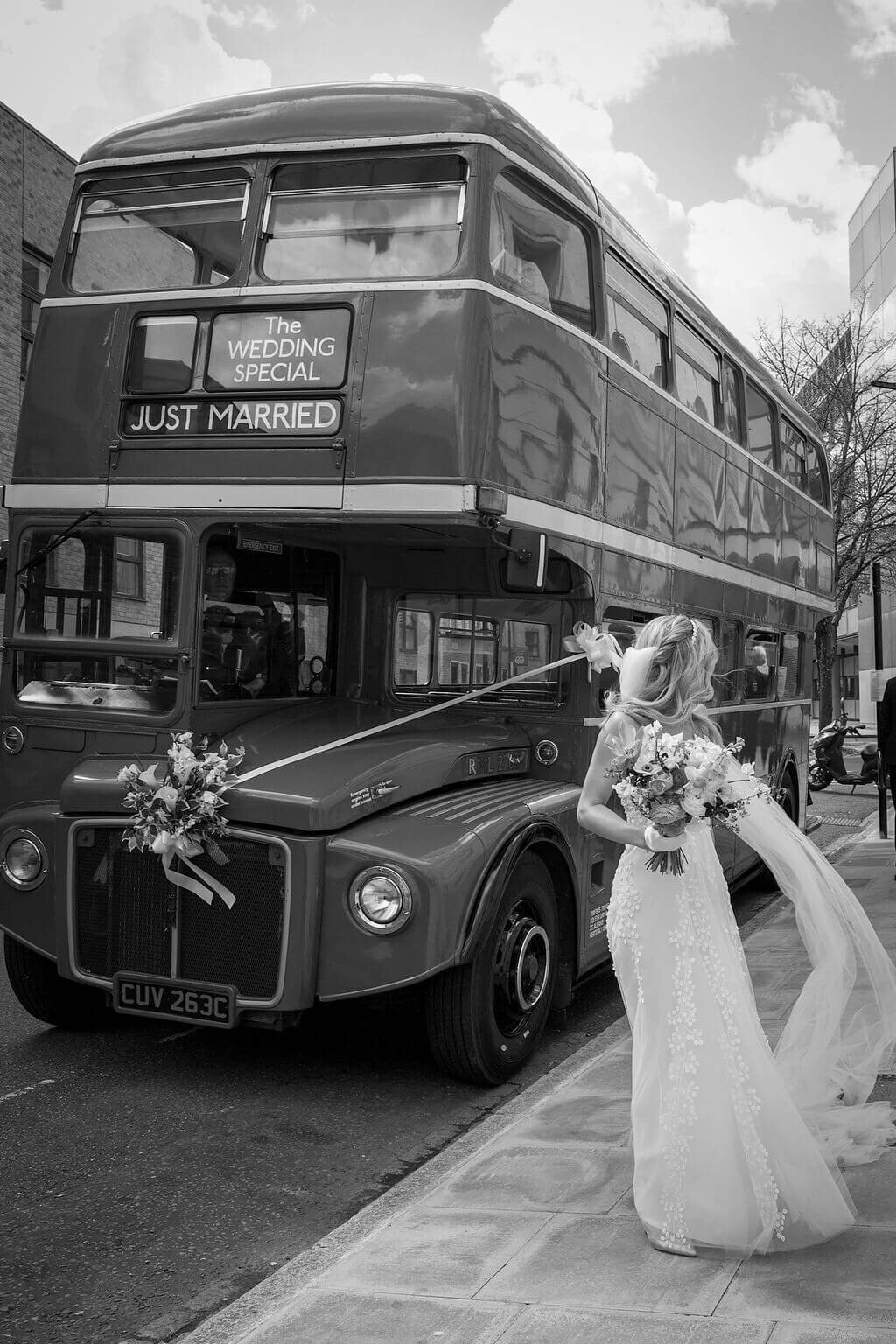 Bride standing next to wedding bus outside Hackney Town Hall