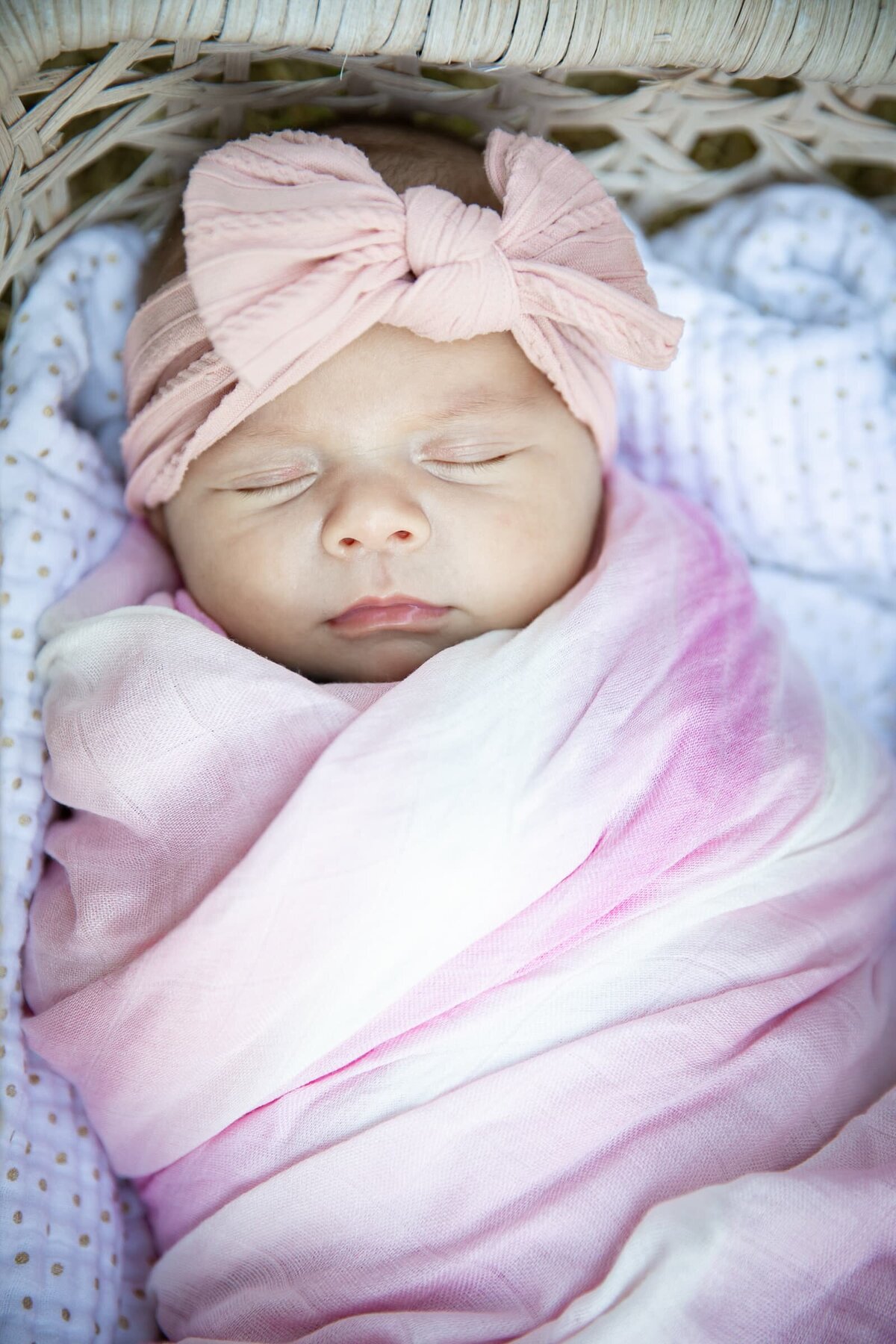 Best newborn photographer in Wake Forest NC. Baby girl sleeping in a woven basket wearing a pink bow and pink wrap. Natural newborn photos.