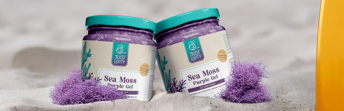 Two mason jars on the beach leaning on one another with purple sea moss on either side. The lids are a sea-green color with branded packing for Just Livity.