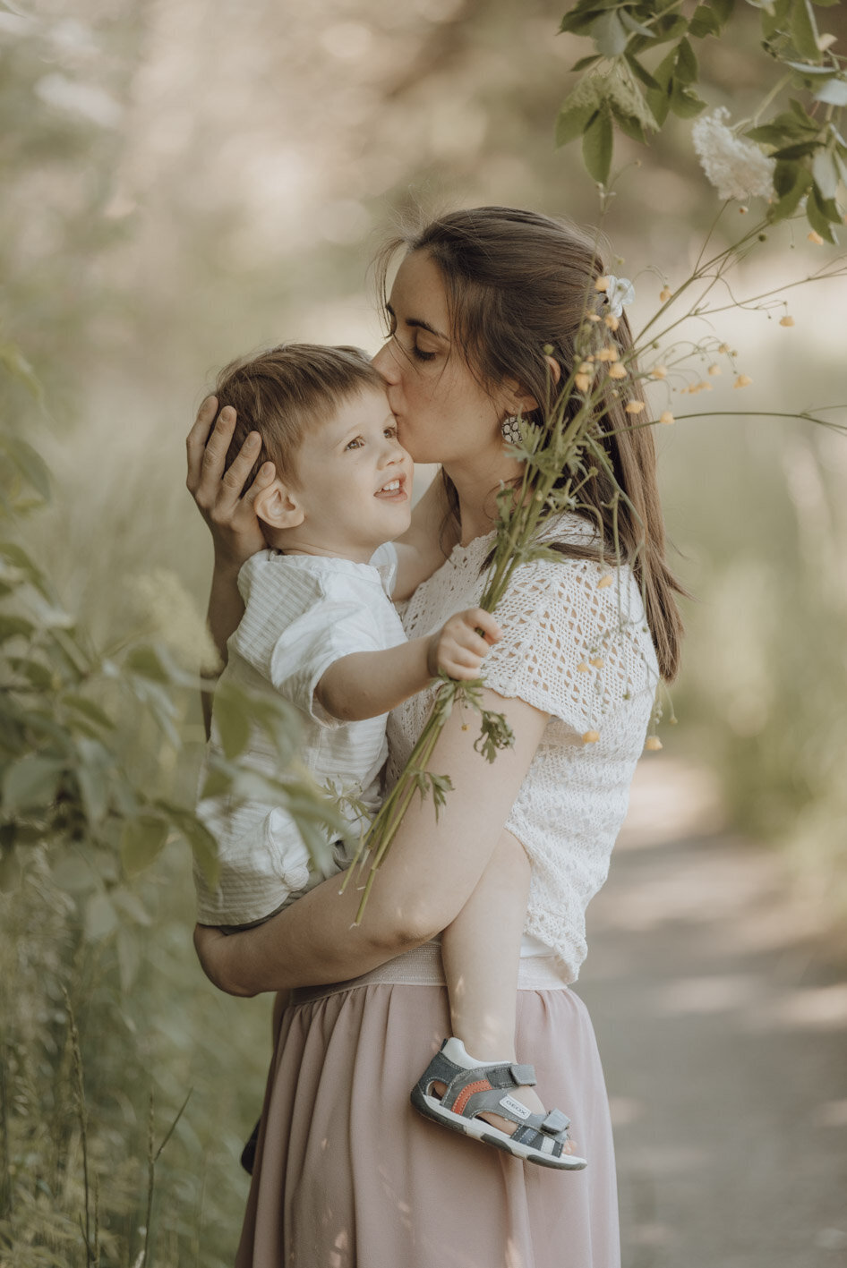Moeder knuffelt zoontje met boterbloemen in zijn hand onder boom