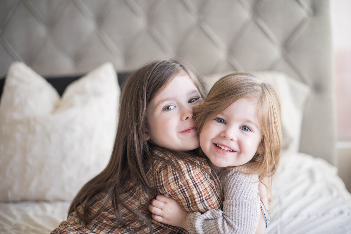 Young sisters joyfully hugging each other while sitting on a bed