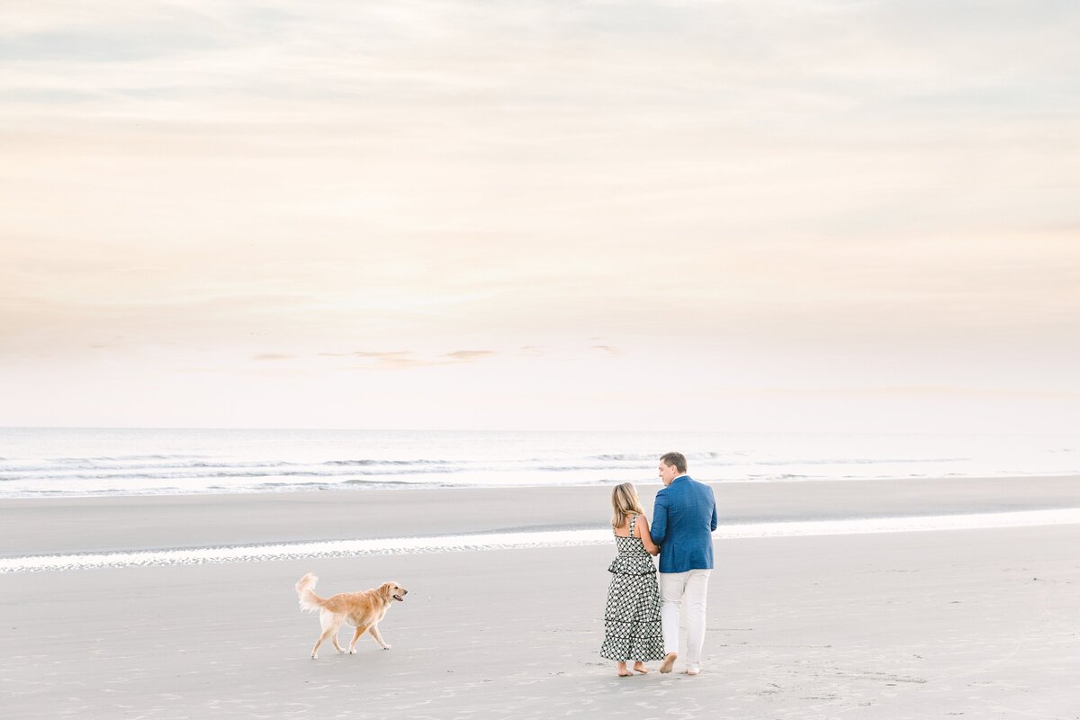 couple walking away together on the beach during sunset with their dog
