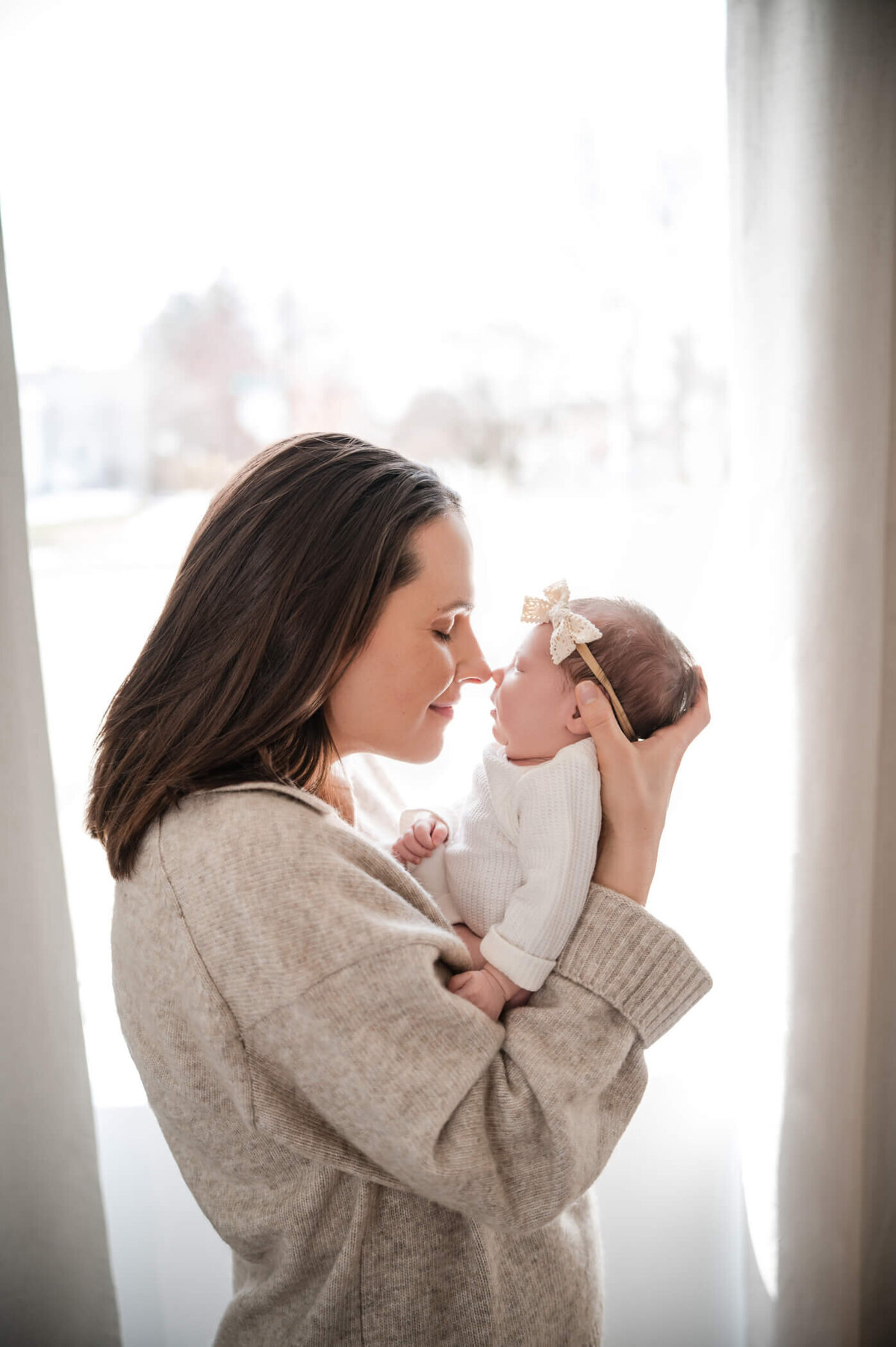 mom holding newborn to her nose in front of a well lit window