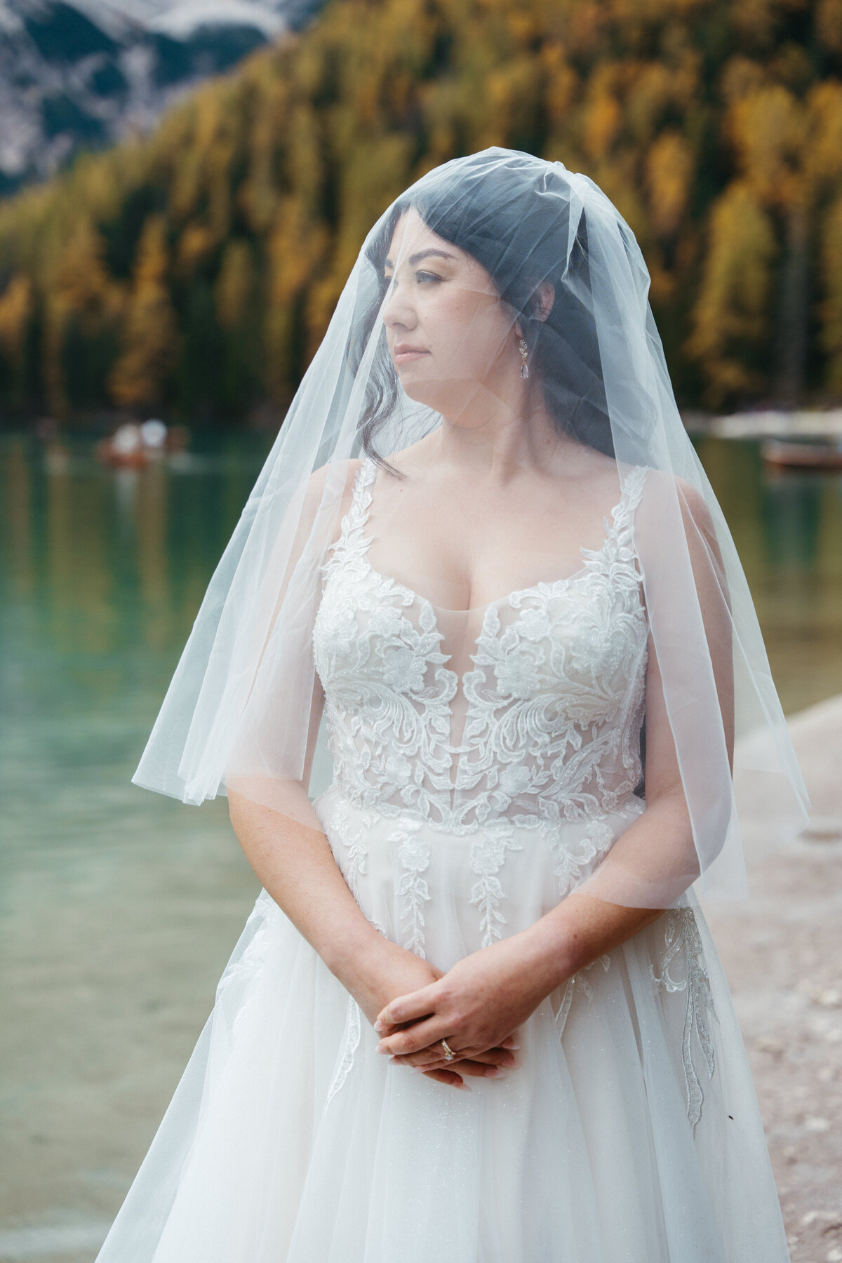 Bride standing by lake wearing veil and lace wedding gown