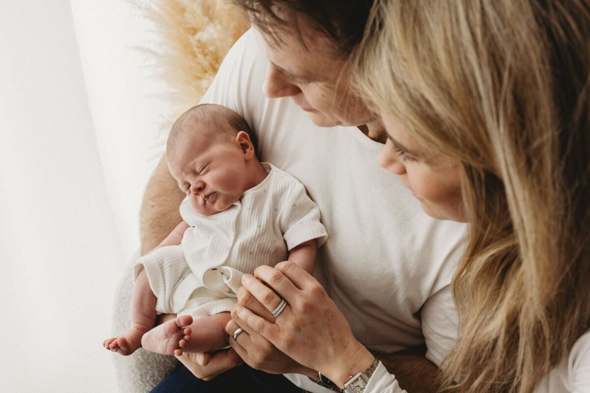 A tender close-up of a new mother and father lovingly gazing at their peacefully sleeping newborn baby, who is nestled in their arm