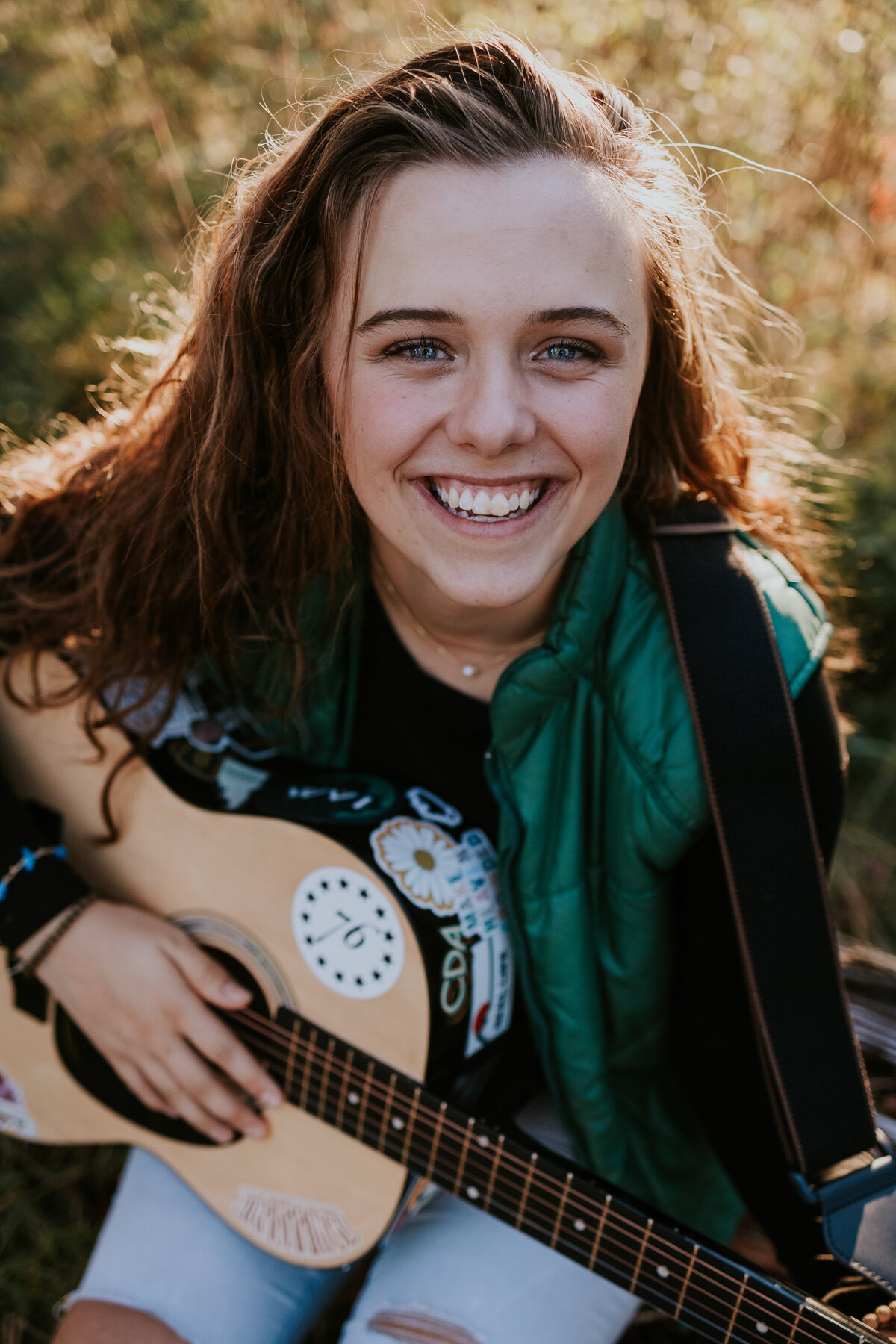 Young woman holding guitar covered in stickers looks up at camera and smiles.
