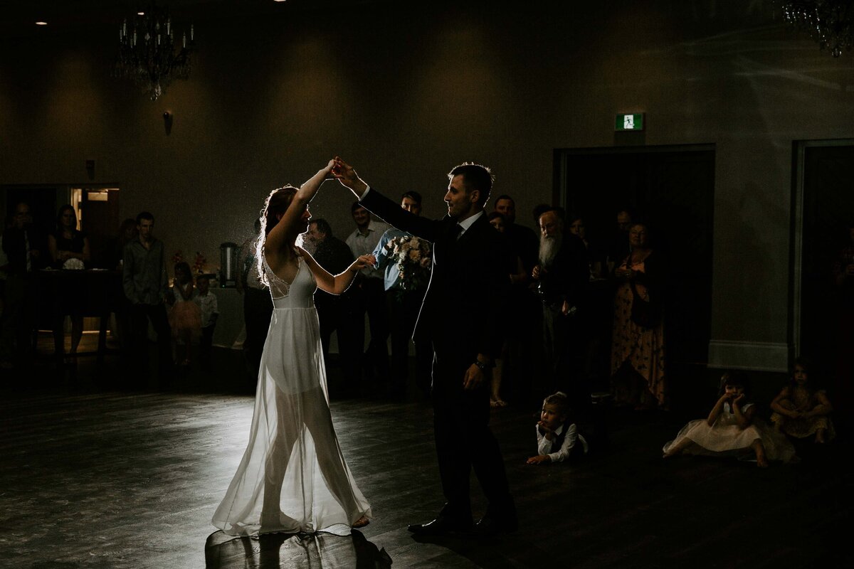 Bride and groom enjoying their first dance at their wedding reception. Bride is in reception dress and barefoot and groom is spinning her on the dance floor.