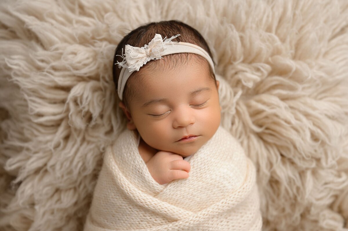 Baby newborn girl in neutral color scheme posed in wrap and headband on fur.