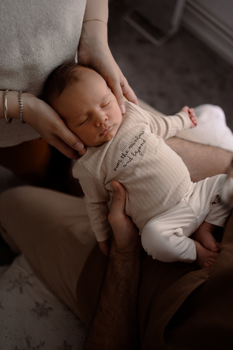 Baby ligt in de handen van vader en moeder terwijl hij slaapt ijdens een newbornshoot