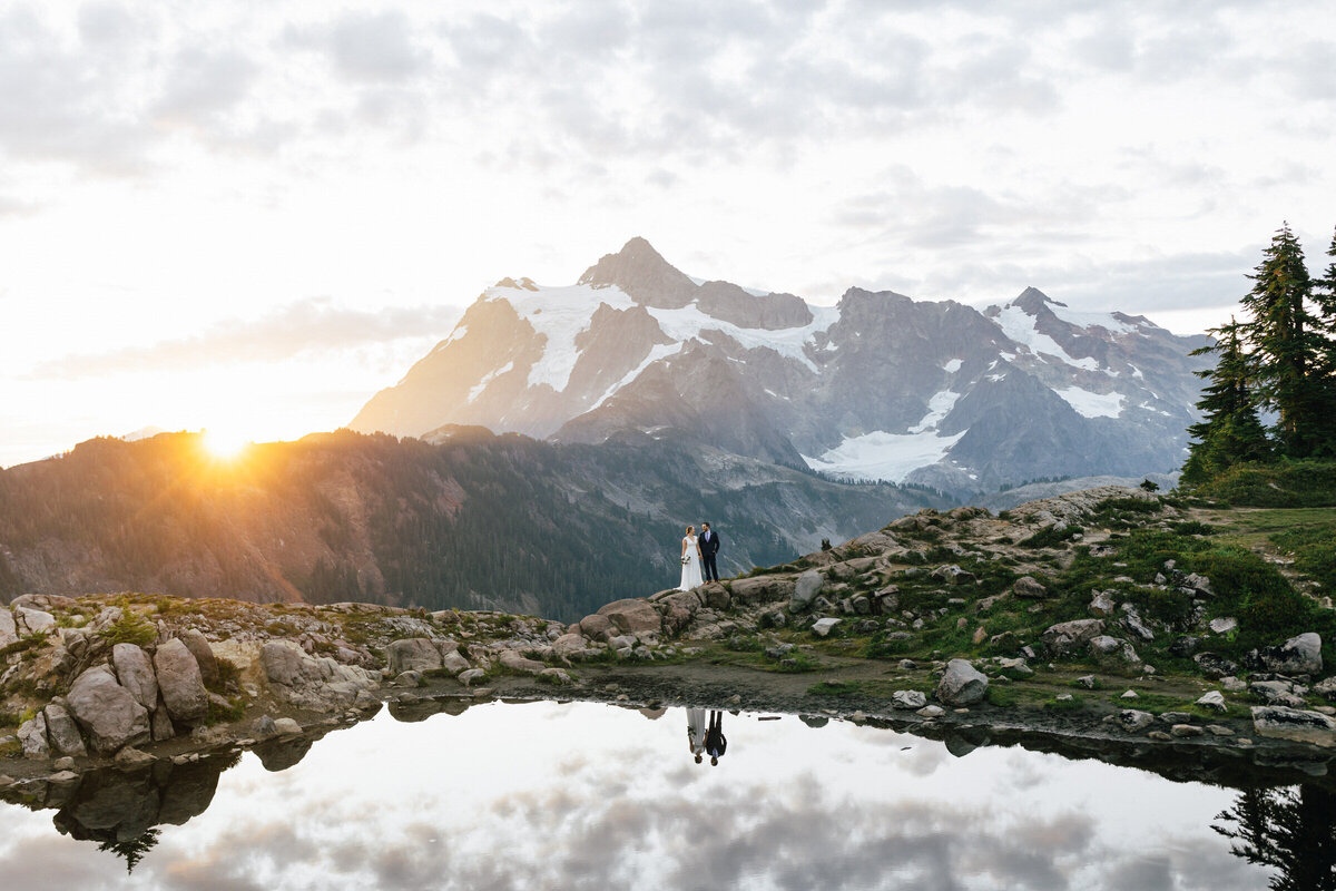 A bride and groom hold hands as the sun rises behind Mt. Shuksan in Washington's North Cascades National Park.