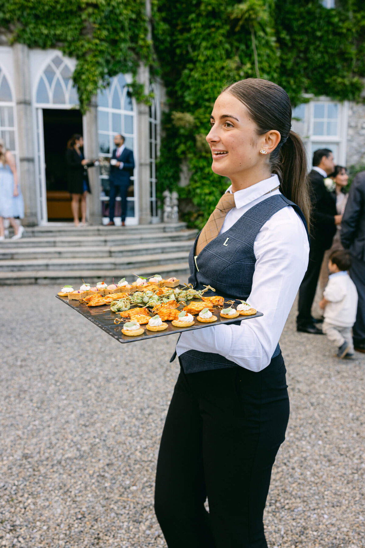 A wedding photo showing a staff member at Luttrellstown Castle in Ireland holding a plate of finger food at cocktail hour