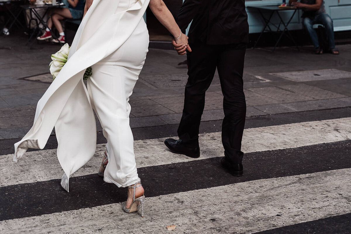 closeup of a bride and groom holding hands crossing a zebra crossing on the streets of london as they walk to their intimate wedding at the nomad hotel