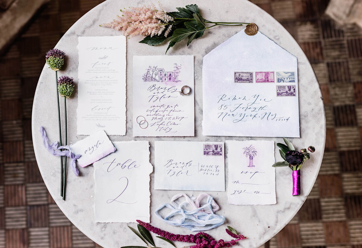 Wedding invitation, envelope with postage stamp & flowers laid out on a round table