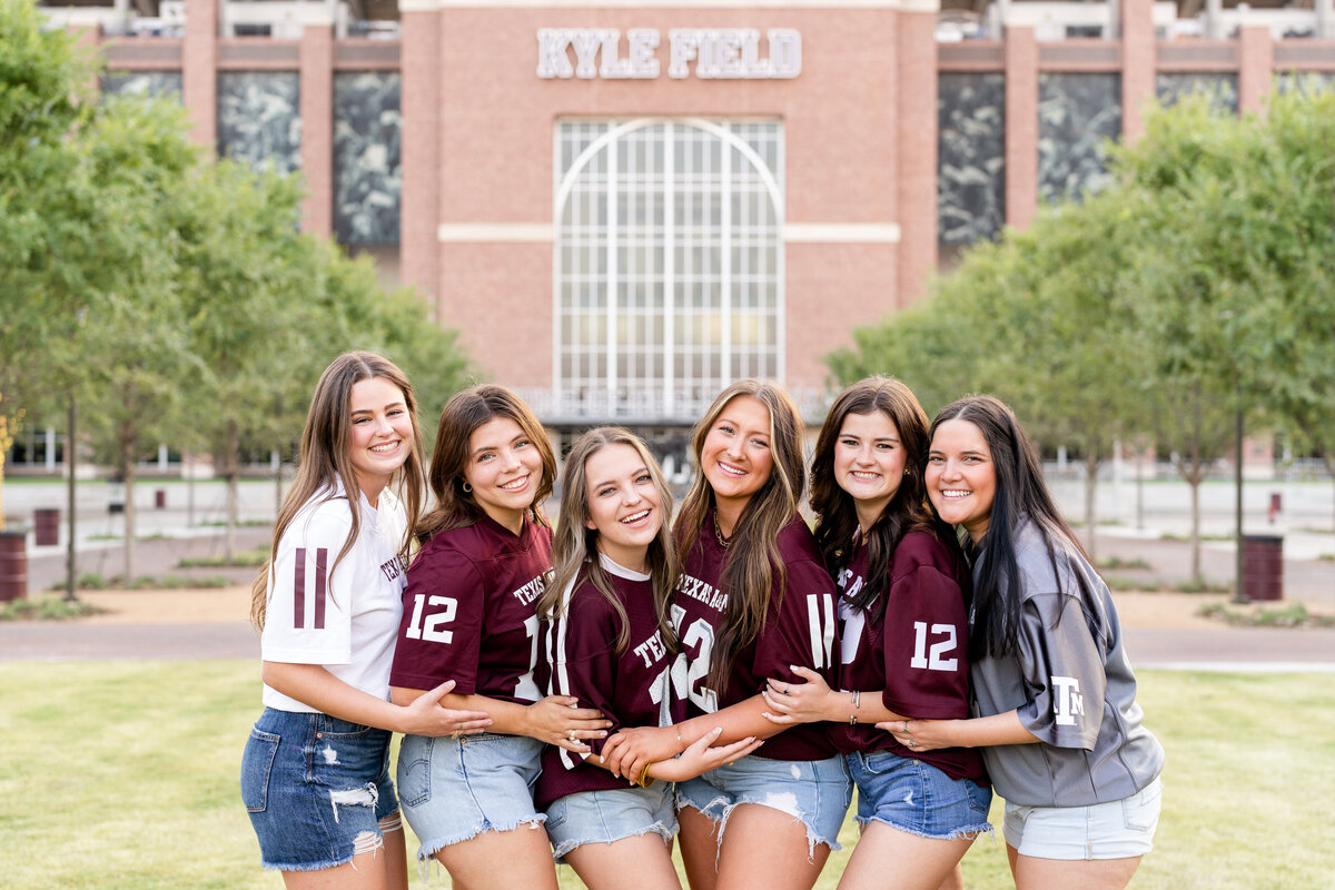 Texas A&M senior girls wearing maroon jerseys and hugging each others in Aggie Park in front of Kyle Field