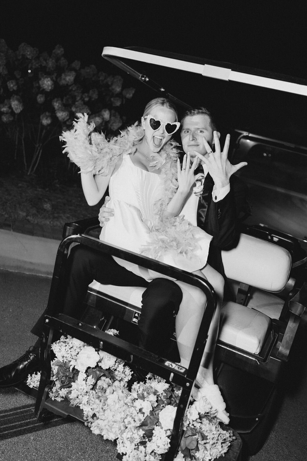 Bride and goom show off rings on back of golf cart leaving reception