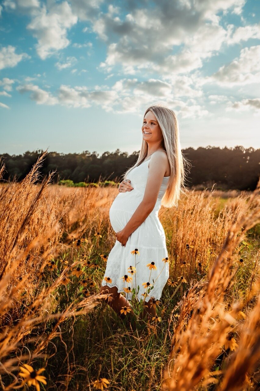 Pregnant woman in a white dress in a field under blue skies
