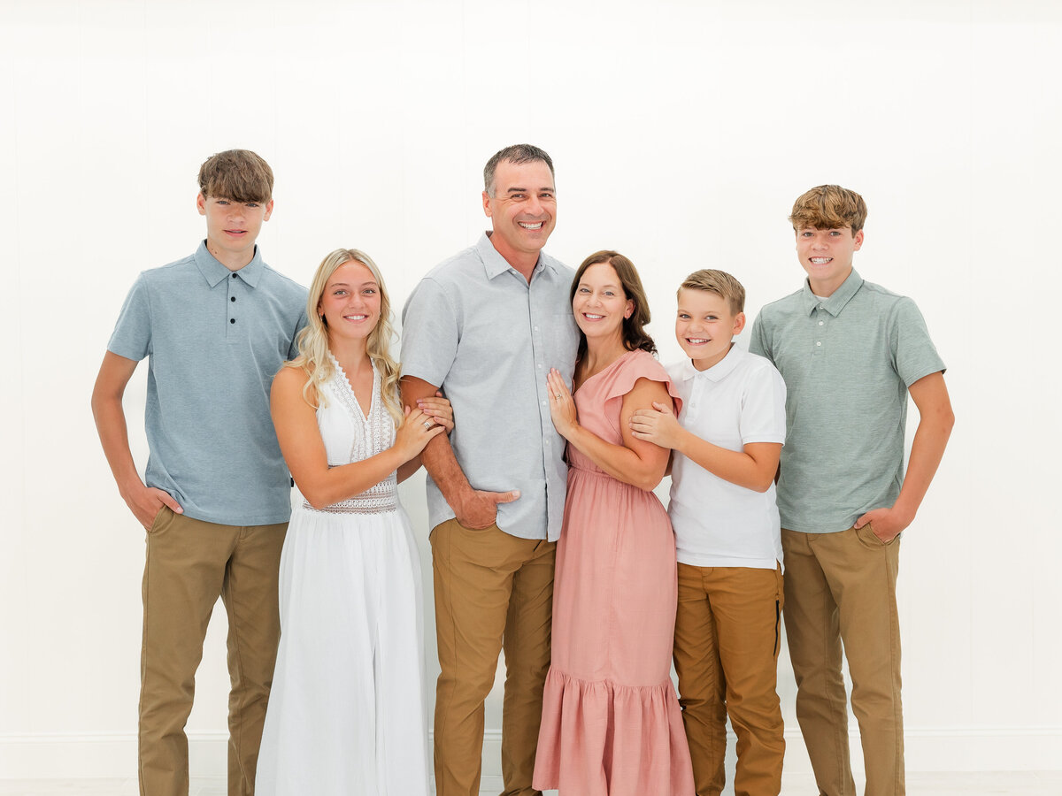 Family standing close and smiling by a white wall for North East, PA, family photography.