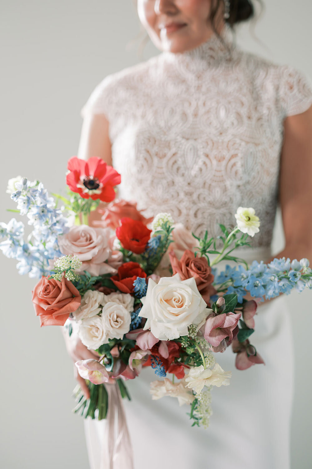 Bridal bouquet with red poppies, ivory and blush roses, and blue accents, captured during a modern wedding inspiration shoot at the Kimpton Armory in Bozeman, Montana.