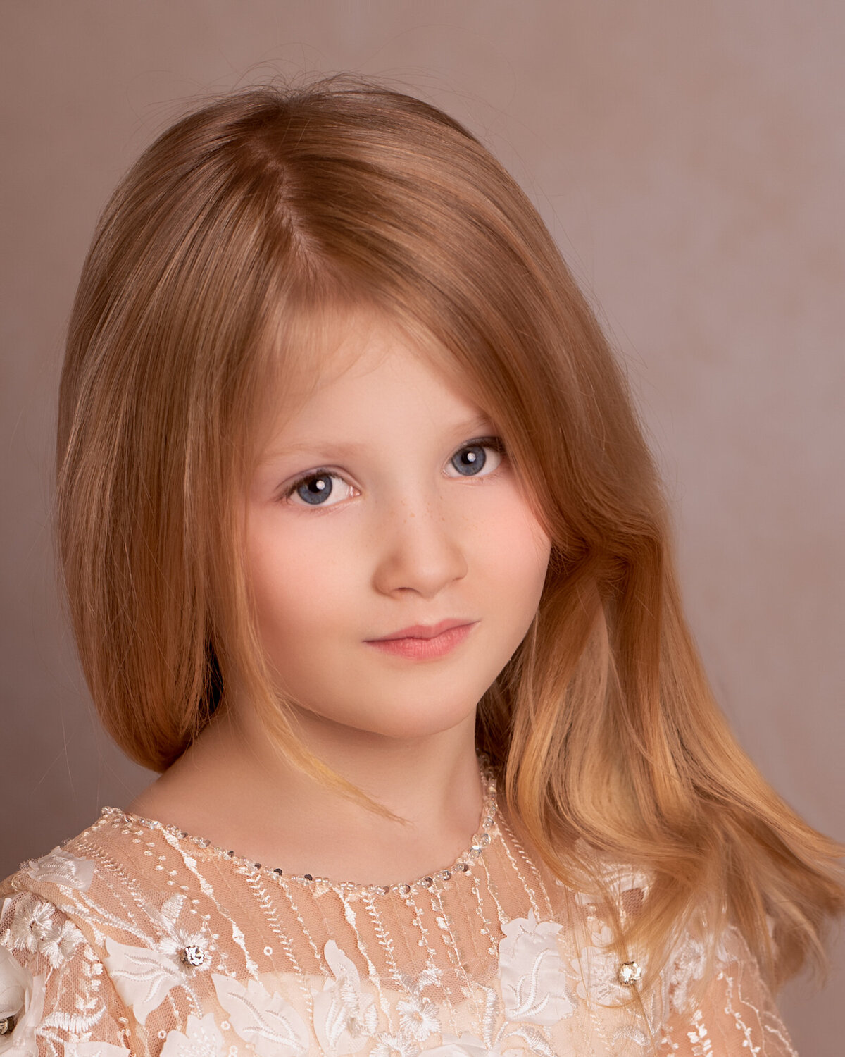 Timeless fine art portrait of a young girl in a delicate lace dress, captured against a warm-toned backdrop. Captured in Overland Park, Kansas, this classic setup is ideal for families seeking elegant and artistic child photography.