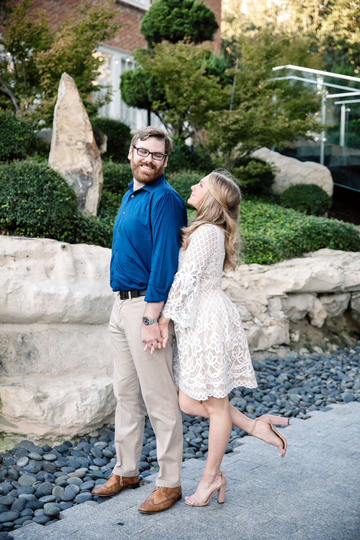Couple in the Harwood District during their engagement session, she leans in from behind as he looks back at her.