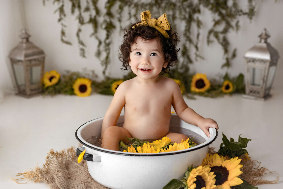 toddler wearing a yellow bow on her head in a bath with sunflowers