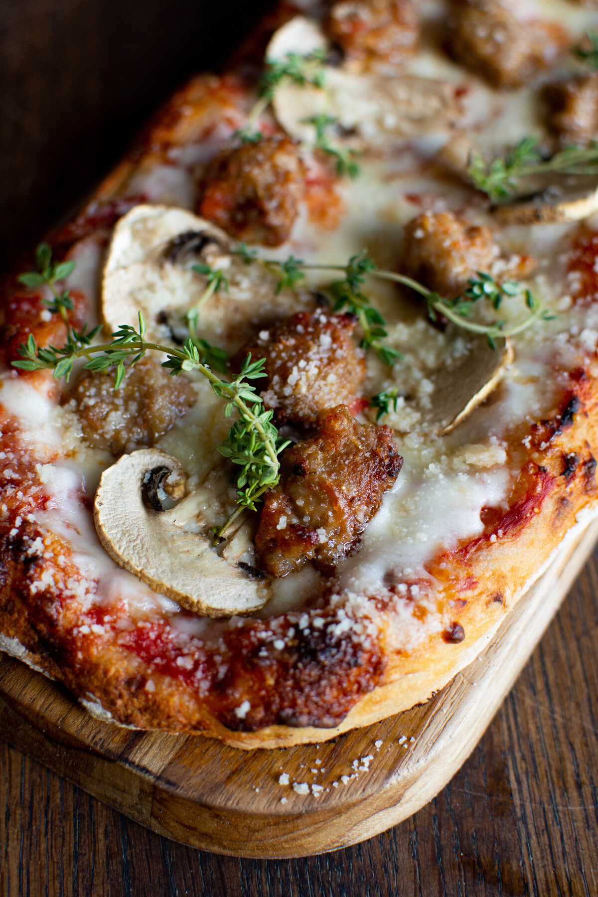 Rustic looking pizza on a cutting board with tomato sauce, mozzarella, mushroom and sausage