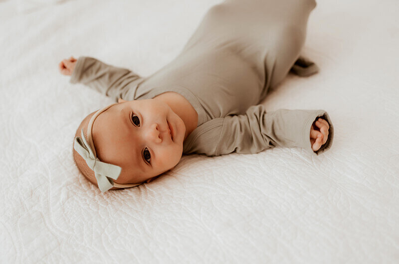 newborn baby girl laying on white knit blanket while wearing an olive green sleeper sack